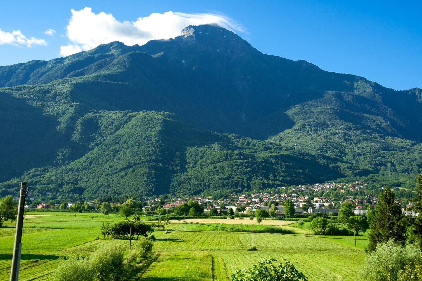 Grüner Weg führt zu einem Steinhaus mit Holzhaus, umgeben von Bergen und Bäumen.