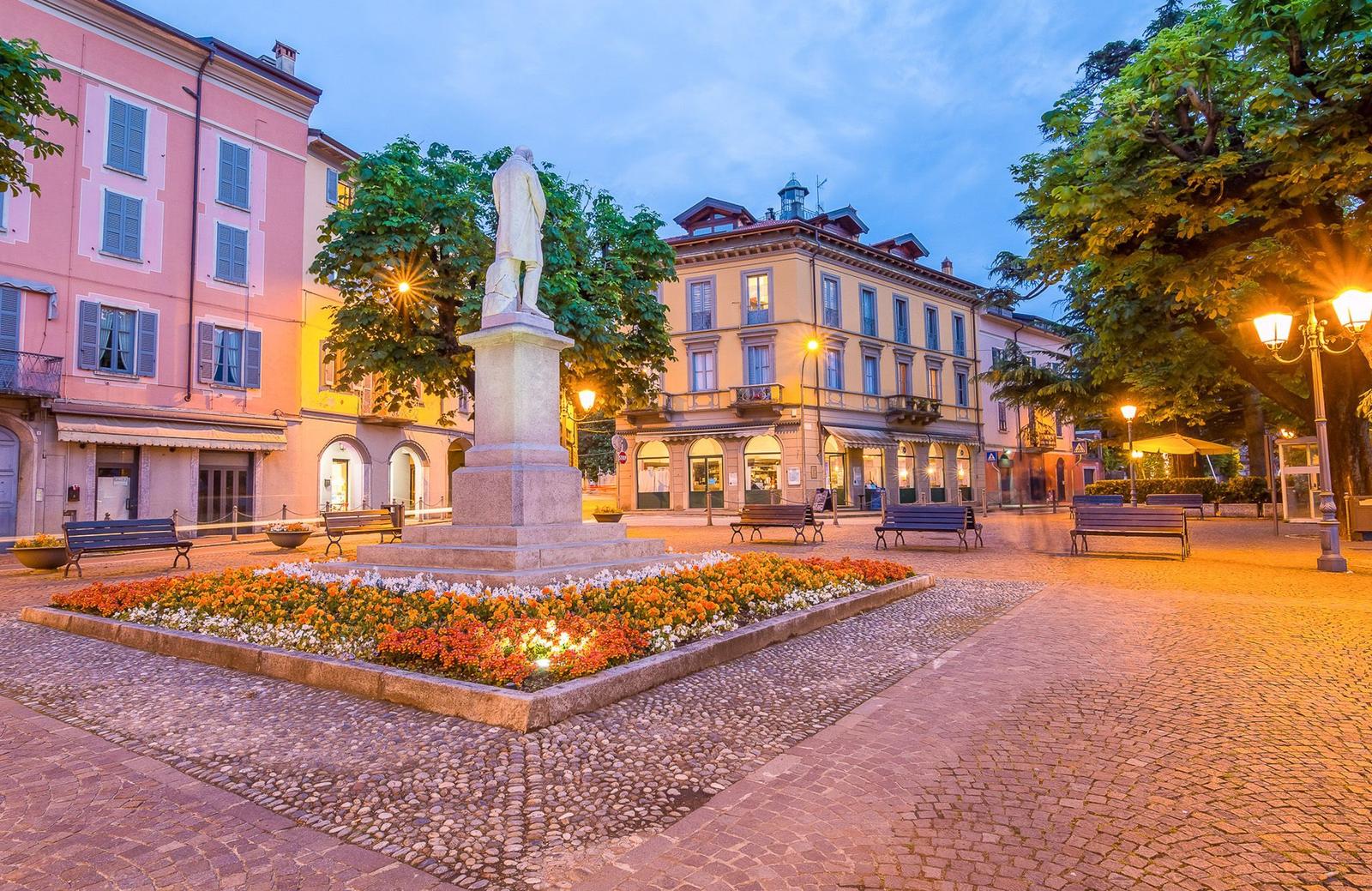 Promenade am Hafen mit Booten und Bergen im Hintergrund.