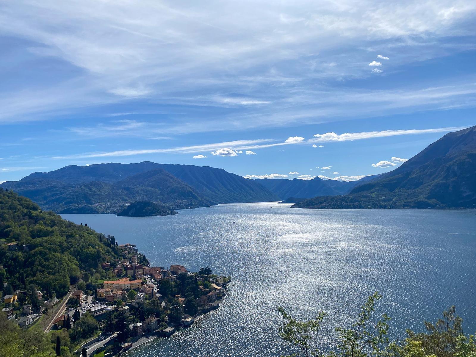 Blick auf einen See mit farbenfrohen Häusern an der Küste und Blumen im Vordergrund.