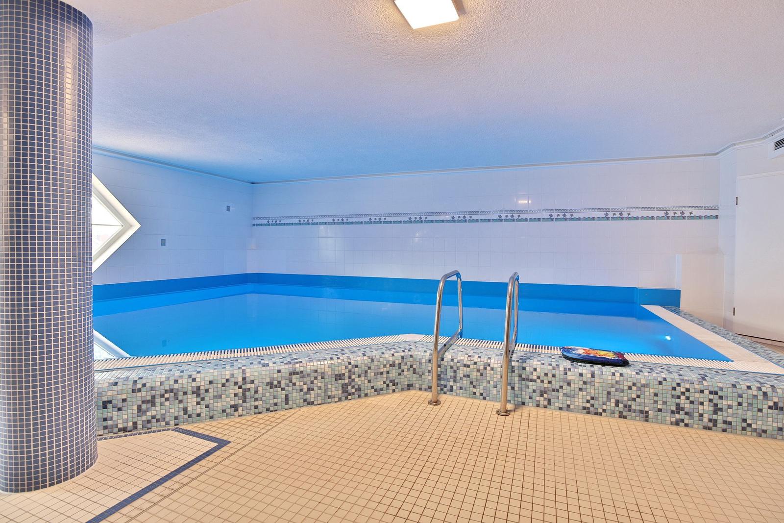 Innenpool mit Sprungbrett, Liegestühlen und dekorativen Fenstern an den Wänden.