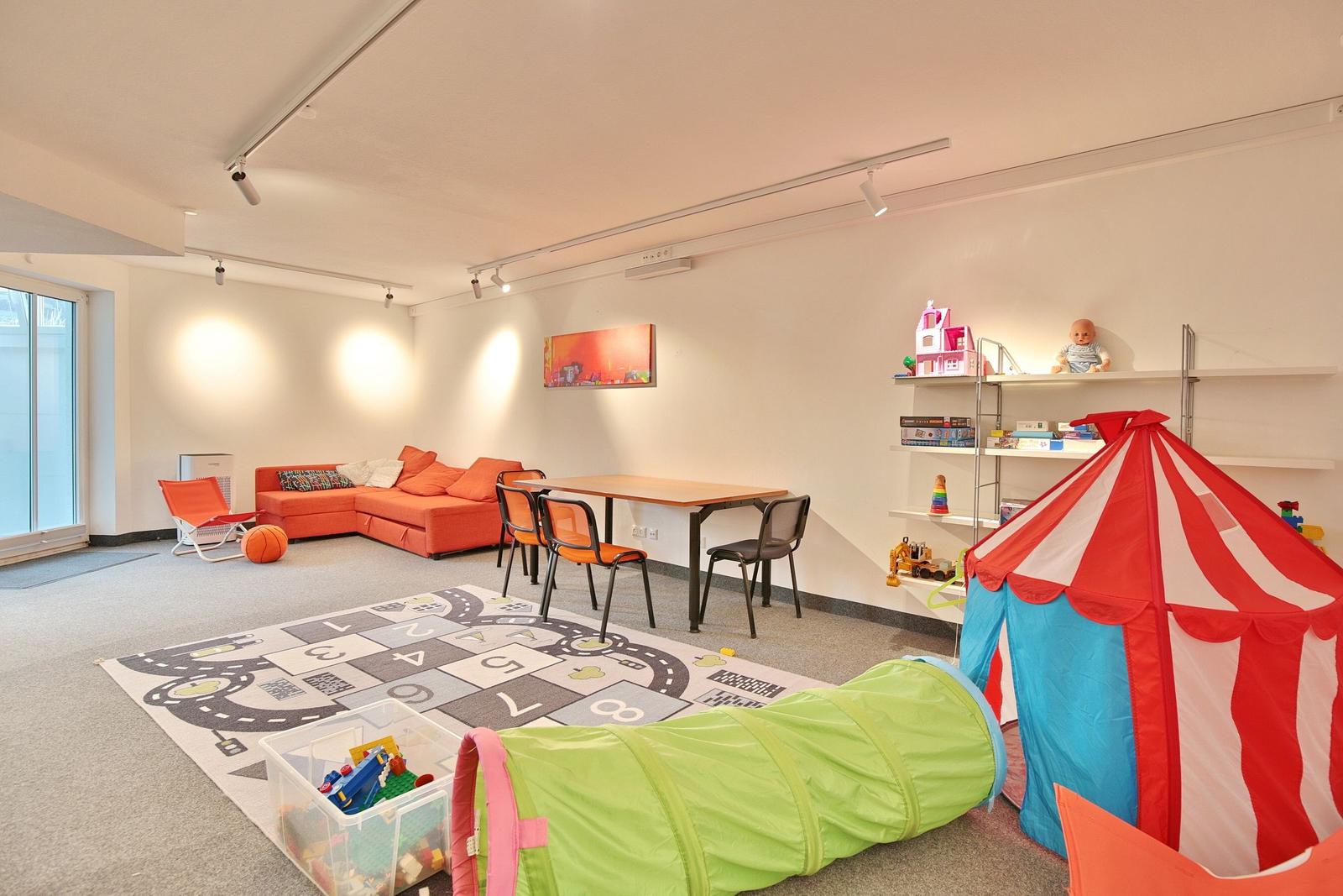 Großer Raum mit Sofa, bunten Aufbewahrungskisten und Kinderbereich mit Tisch und Stühlen.