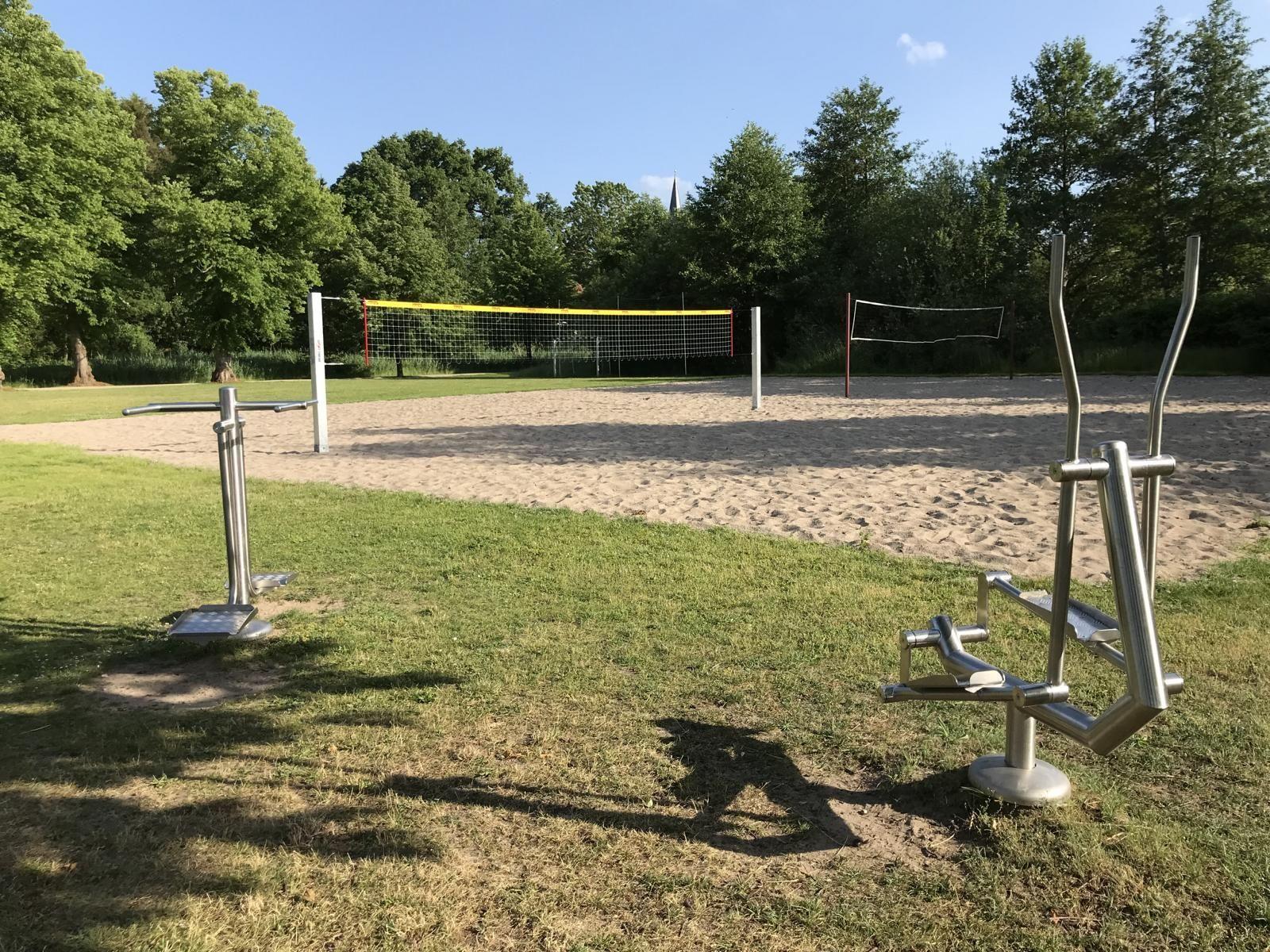 Rotes Klettergerüst auf Sandstrand neben Wasser und Bäumen.