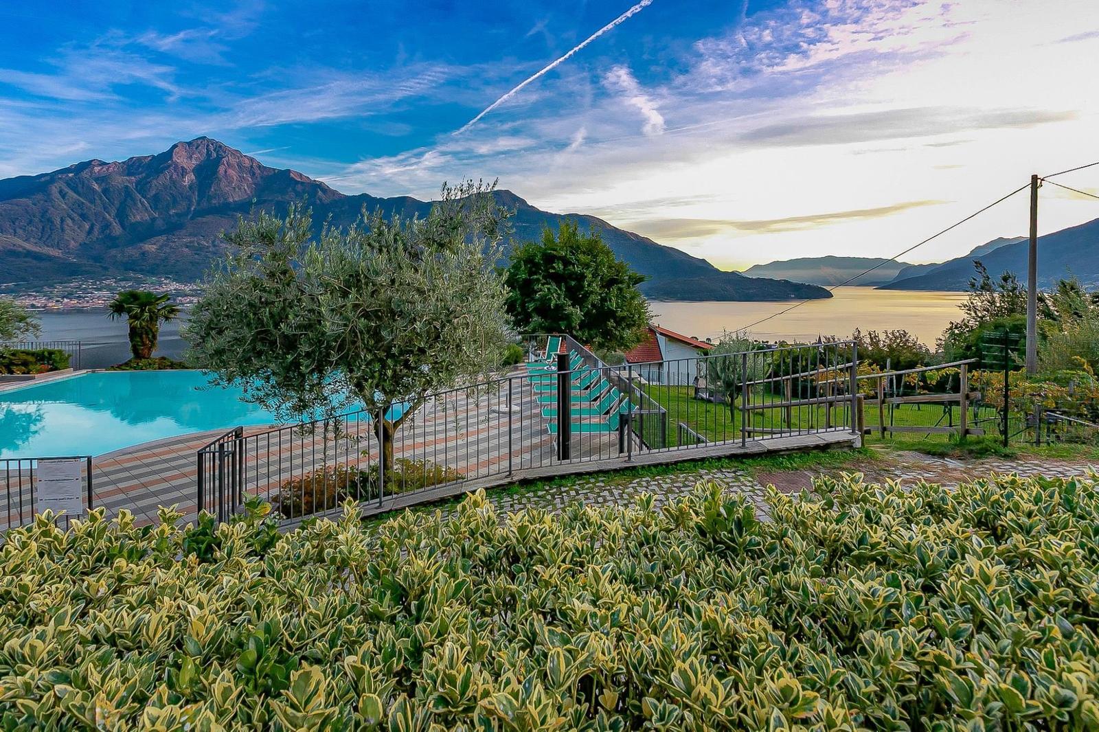 Grüner Garten mit Tisch, Bank und Grill. Blick auf See und Berge.