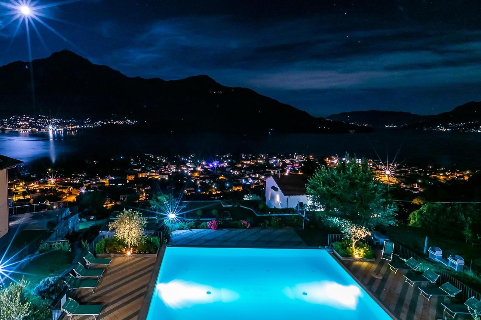 Pool mit Blick auf See und Berge. Grünflächen und Bäume umgeben die Terrasse.