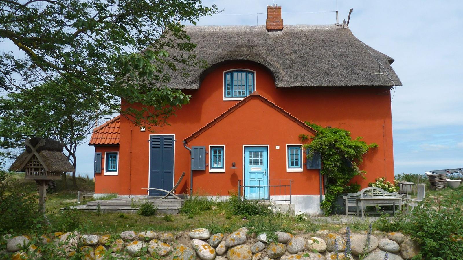 Blauer Strandhaus mit Strohdach und roten Fensterläden direkt am Wasser.