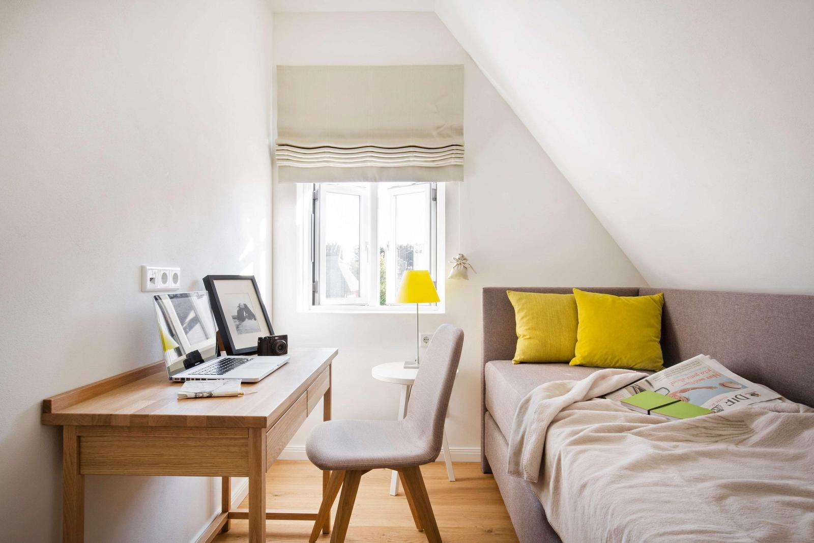 Schlafzimmer mit Bett, Kissen, Decke, Nachttischlampe und Bank mit Koffer und Tasche.