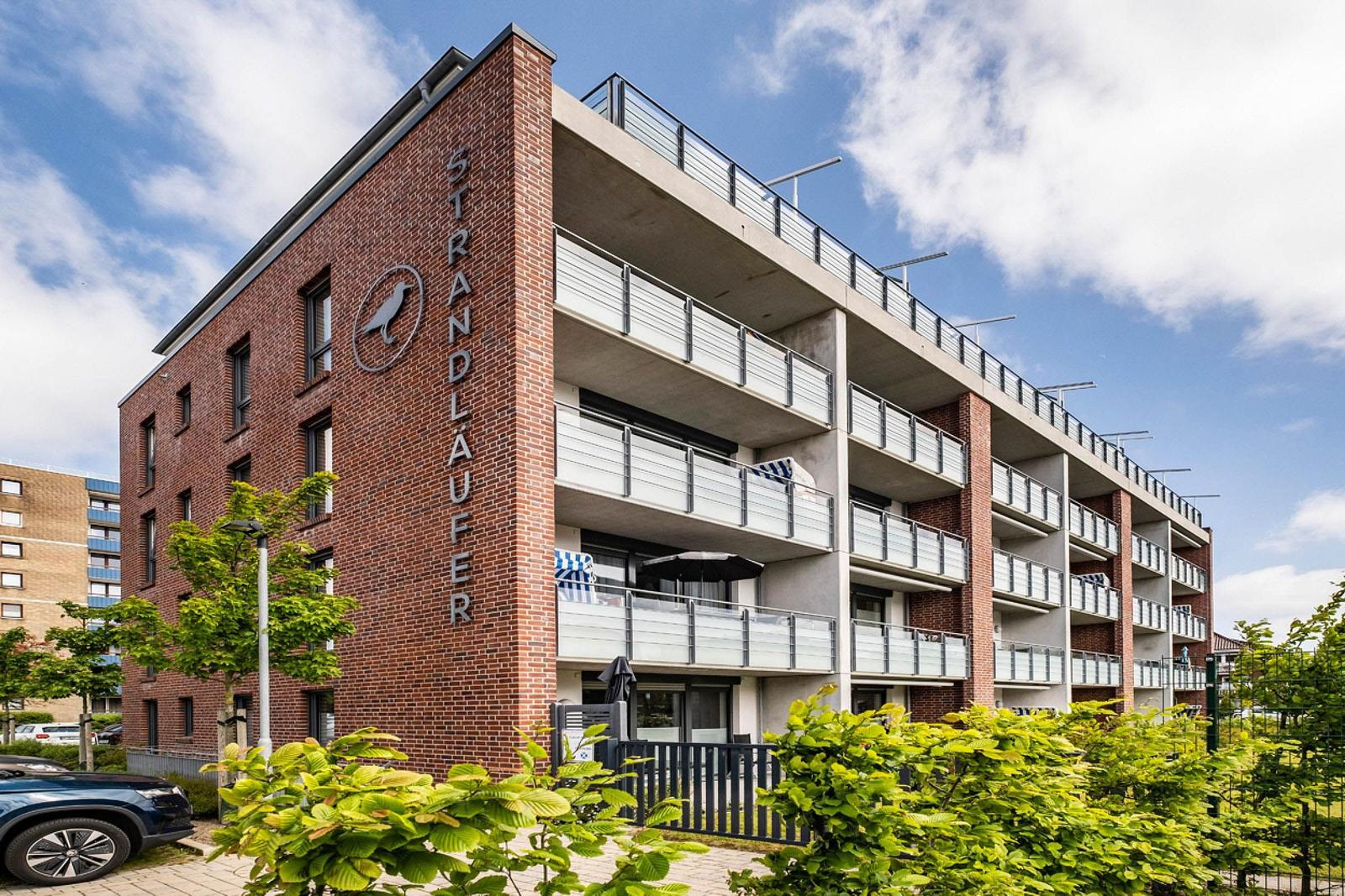 Moderne Wohnanlage mit Balkonen und grüner Hecke. Parkplatz vor dem Gebäude.