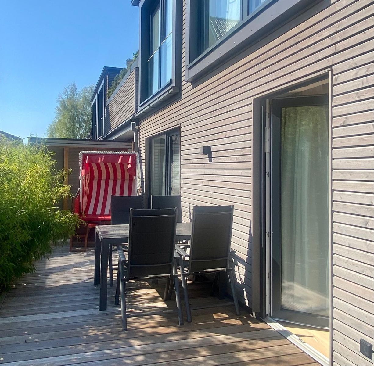 Modernes Haus mit Garten, Grill und Blühbaum unter blauem Himmel.