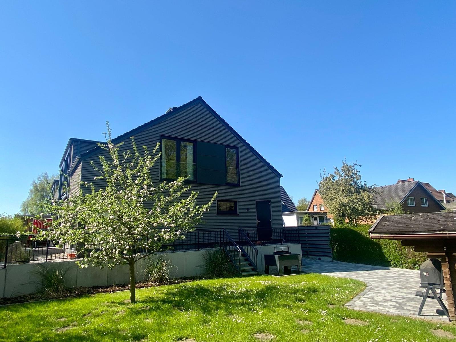 Grüner Garten mit blühendem Baum, Grillplatz und Holzhaus. Sonniger Tag mit viel Grün.