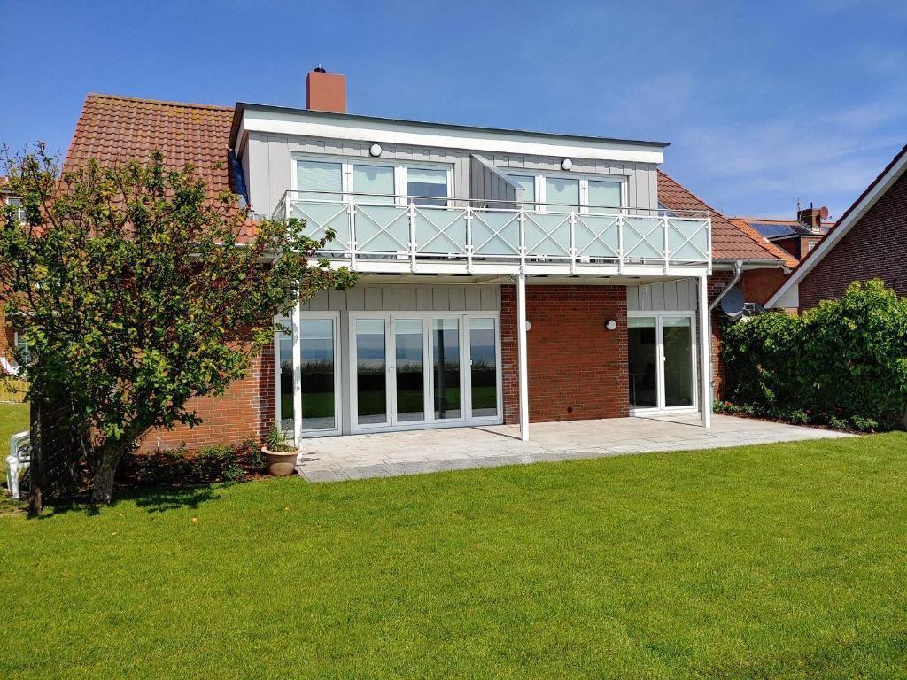 Haus mit Balkon, Glasfront und Garten. Modernes Design mit rotem Dach und weißen Fenstern.