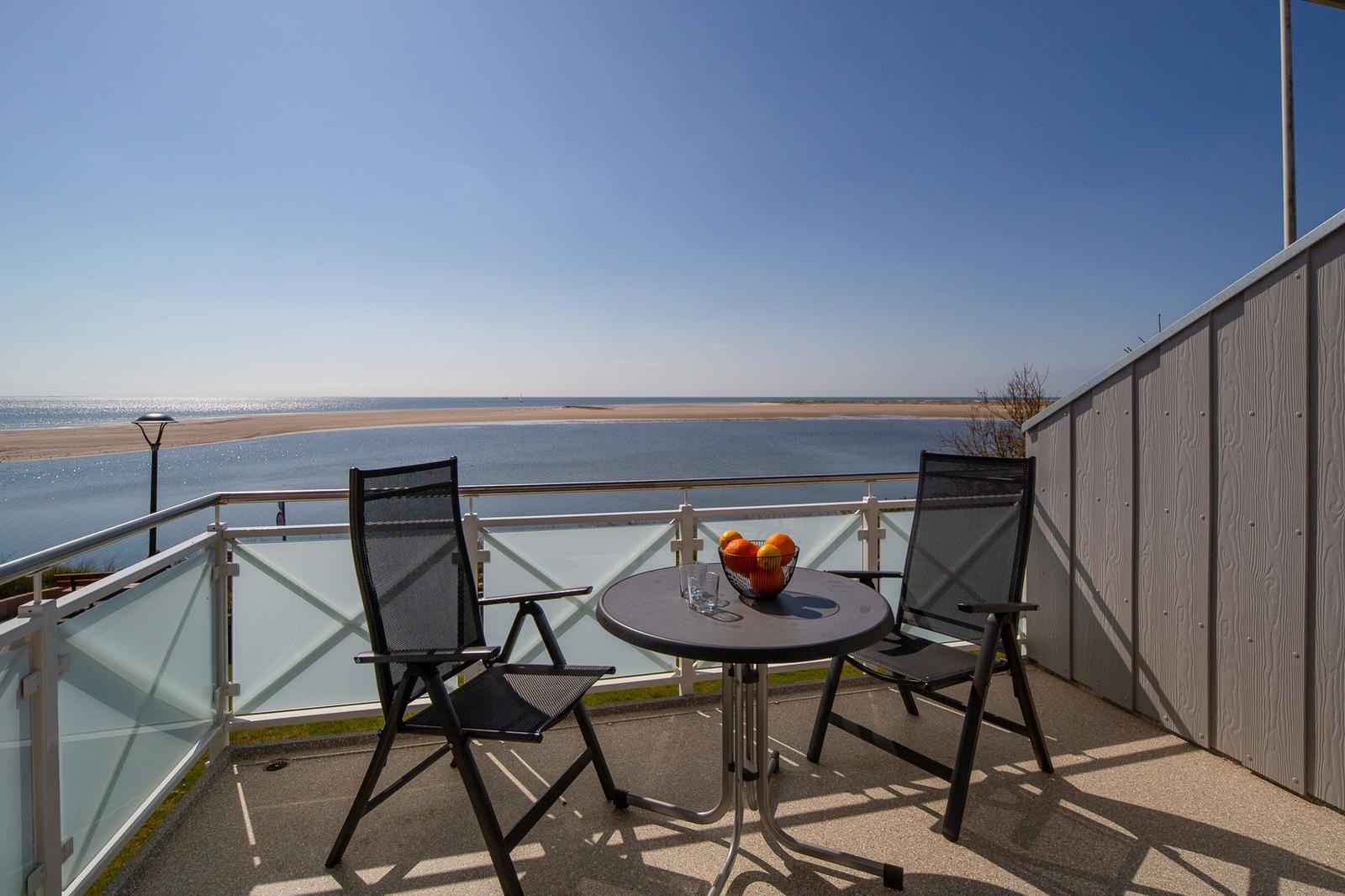 Terrasse mit Tisch und Stühlen. Im Hintergrund Wohnzimmer mit Esstisch und Fernseher.