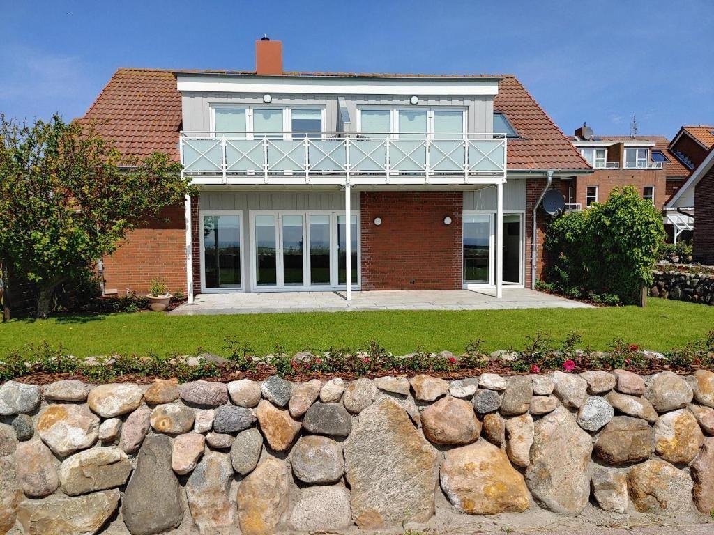 Modernes Haus mit Balkon, Terrasse und Steinmauer im Vordergrund.