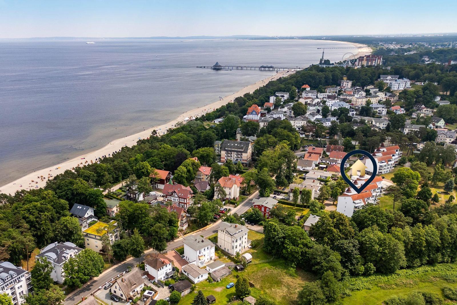 Strand mit Steinschwellen, Steg und Leuchtturm bei Sonnenuntergang.