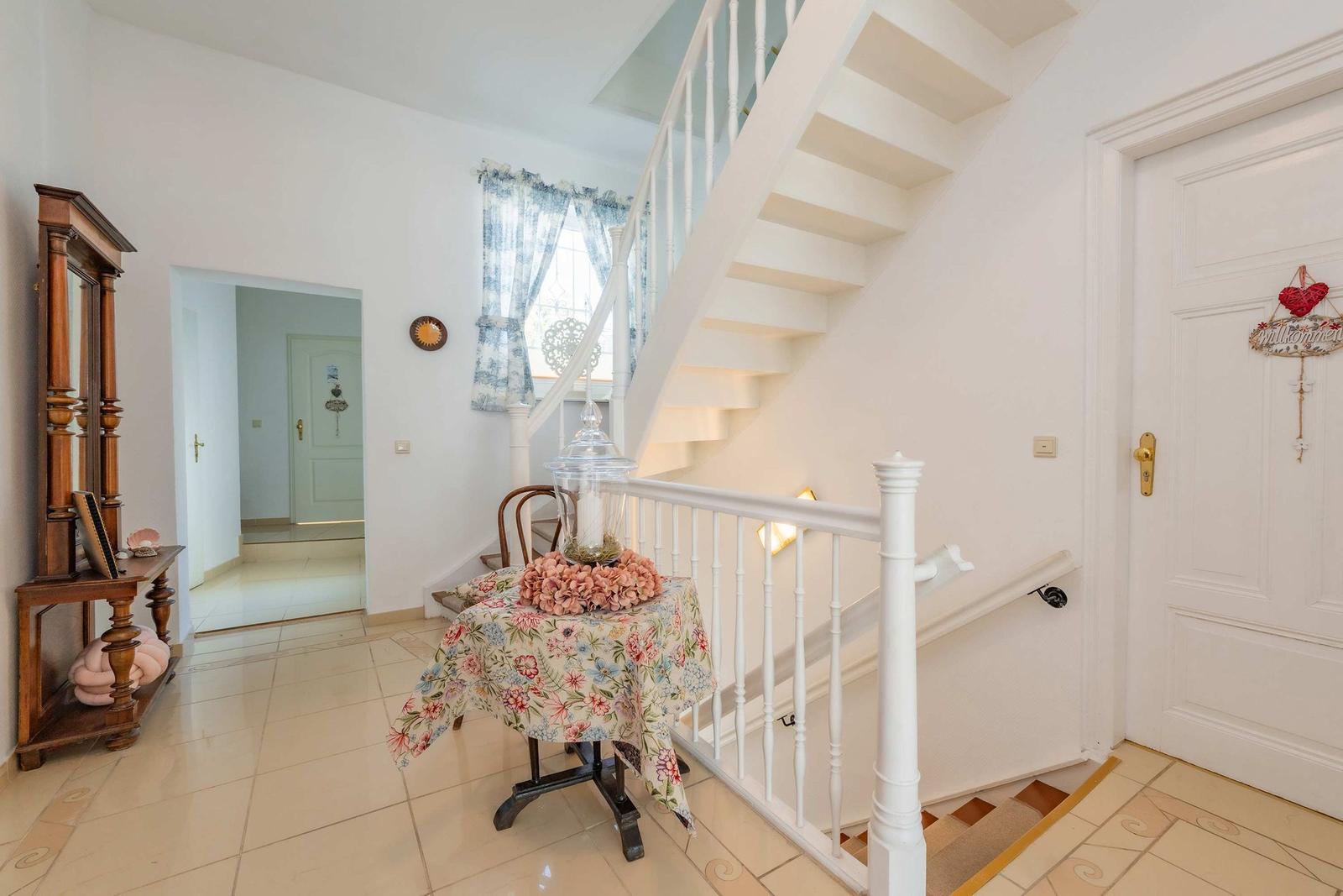 Hallway with staircase, table, and wooden cabinet. Door and wall decor visible.