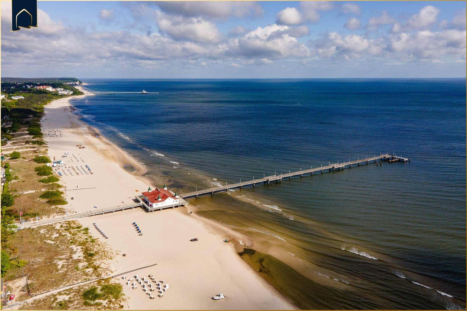Sonnenuntergang am Strand mit Pier und Strandhaus im Hintergrund.