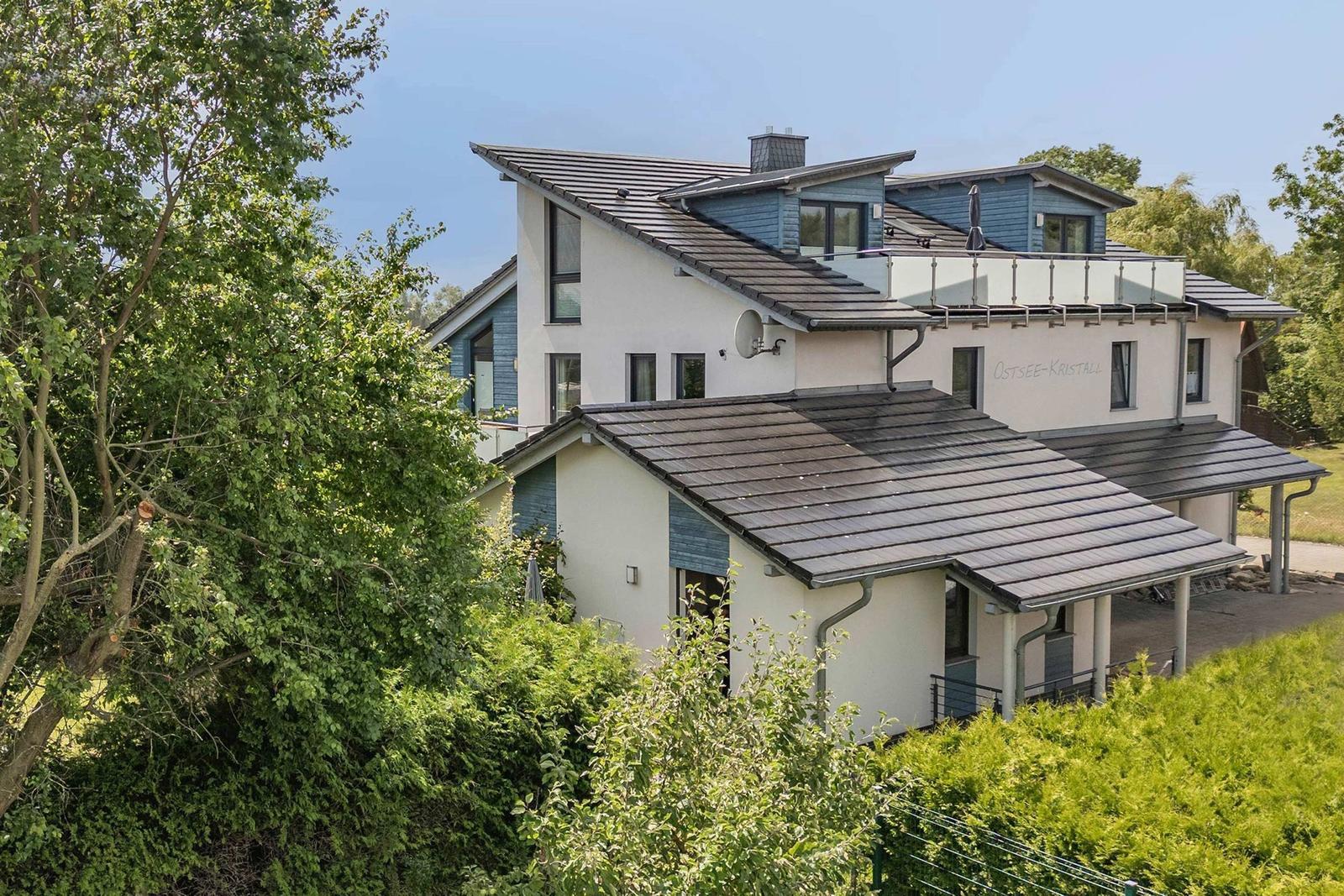 Moderne Villa mit Balkon, umgeben von Grünflächen und Blick auf das Dorf.