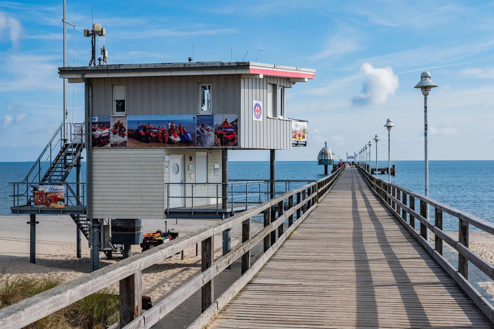 Strand mit Pier und Kuppelhaus im Hintergrund unter blauem Himmel.