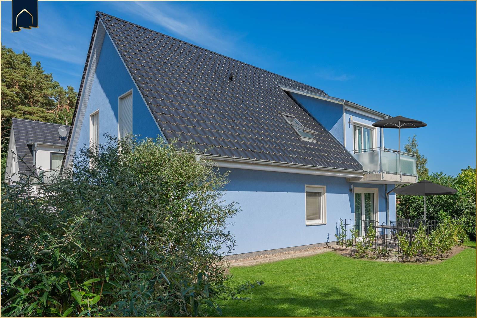 Blau gestrichenes Haus mit Balkon und Gartenbereich unter einem klaren Himmel.