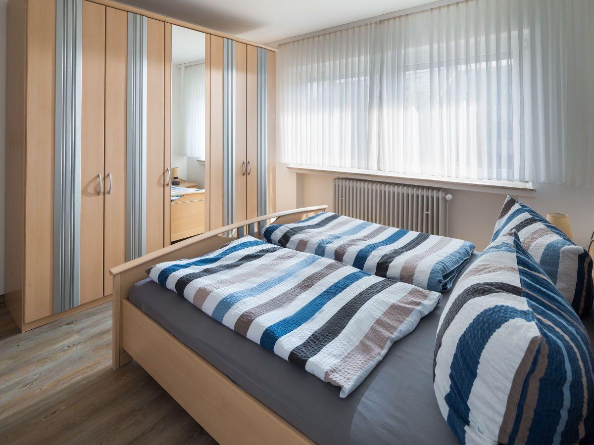 Wohn- und Essbereich mit Sofa, Esstisch und Küchenzeile. Fenster mit weißen Vorhängen.