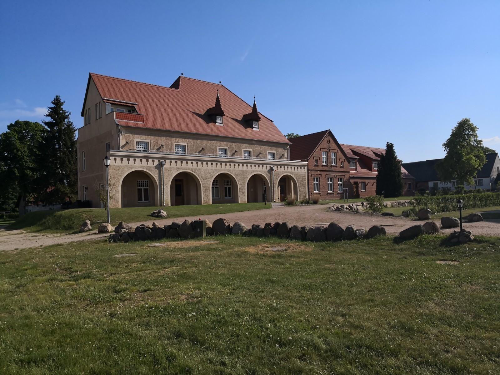 Haus mit rotem Dach, gepflasterter Weg und grünem Rasen vor einem sonnigen Himmel.