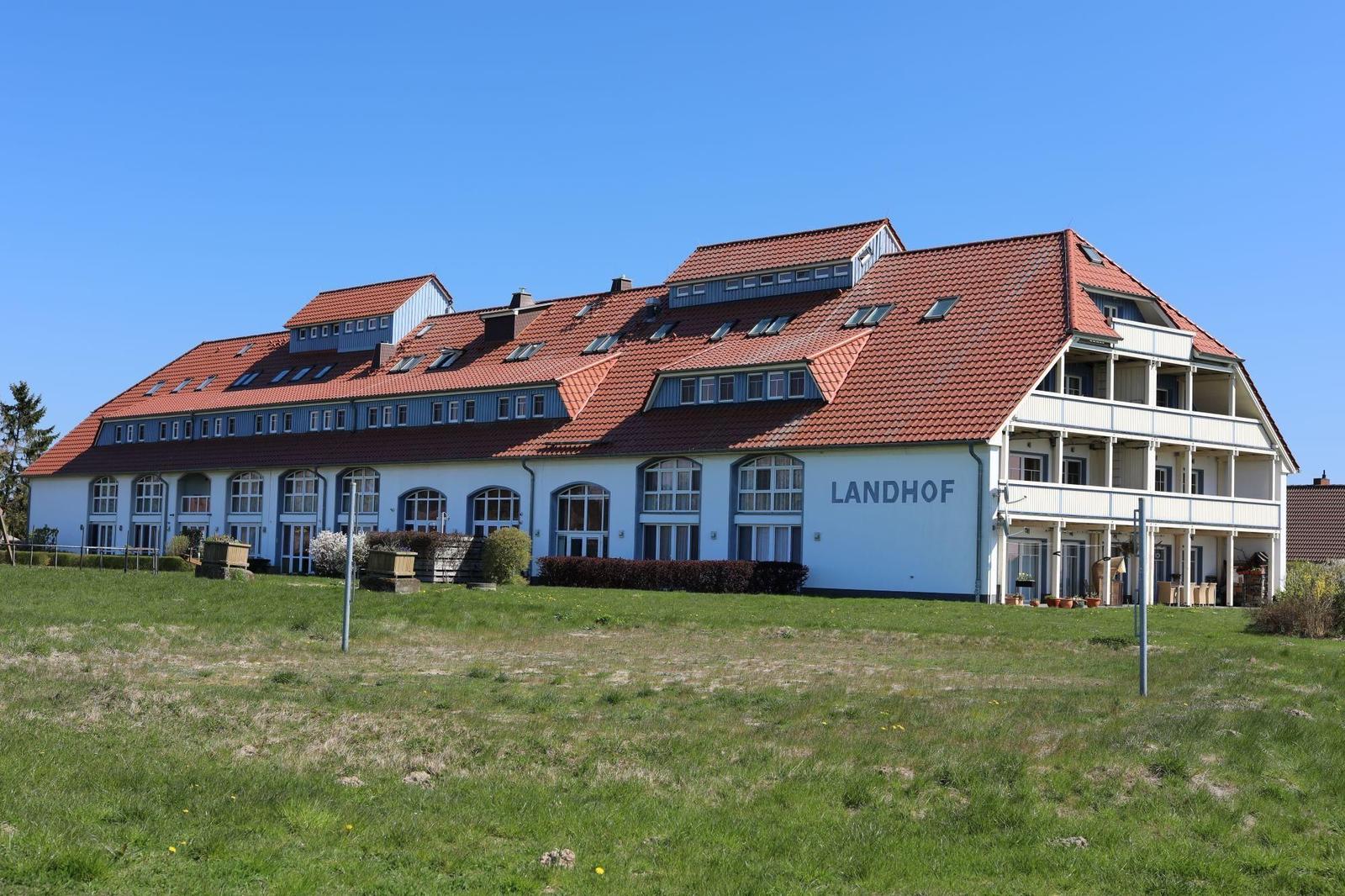 Landhof mit weißen Wänden, rotem Dach und großen Fenstern. Grünhecken säumen den Weg.