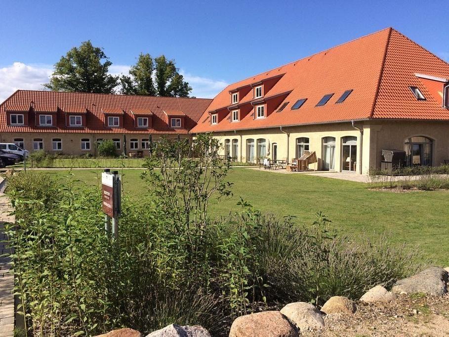 Ein großes Haus mit rotem Dach und Steinmauer. Außenbereich mit Tischen und Sonnenschirmen.