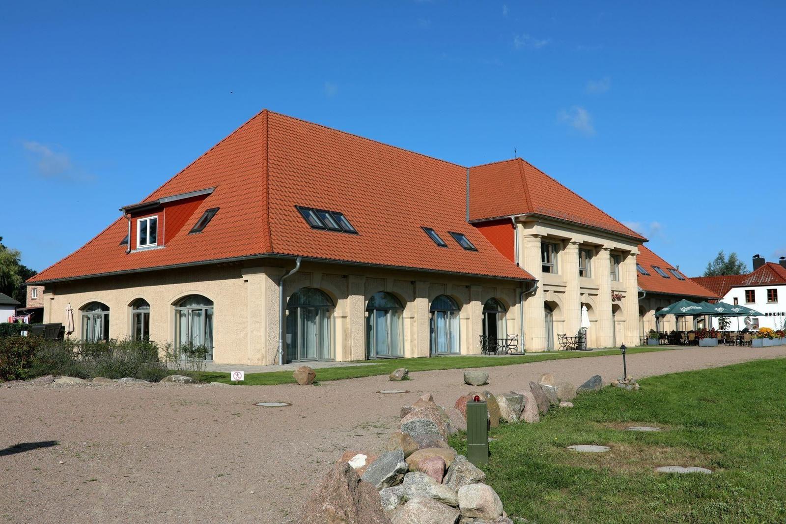 Eingangsbereich mit Säulen und Glasfront. Außenbereich mit Tischen und Stühlen. Dach mit Dachfenstern.