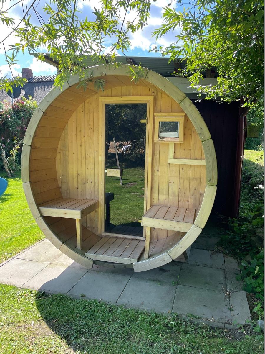 Holzsauna mit Sitzbänken, Ofen und Eimer mit Löffel.