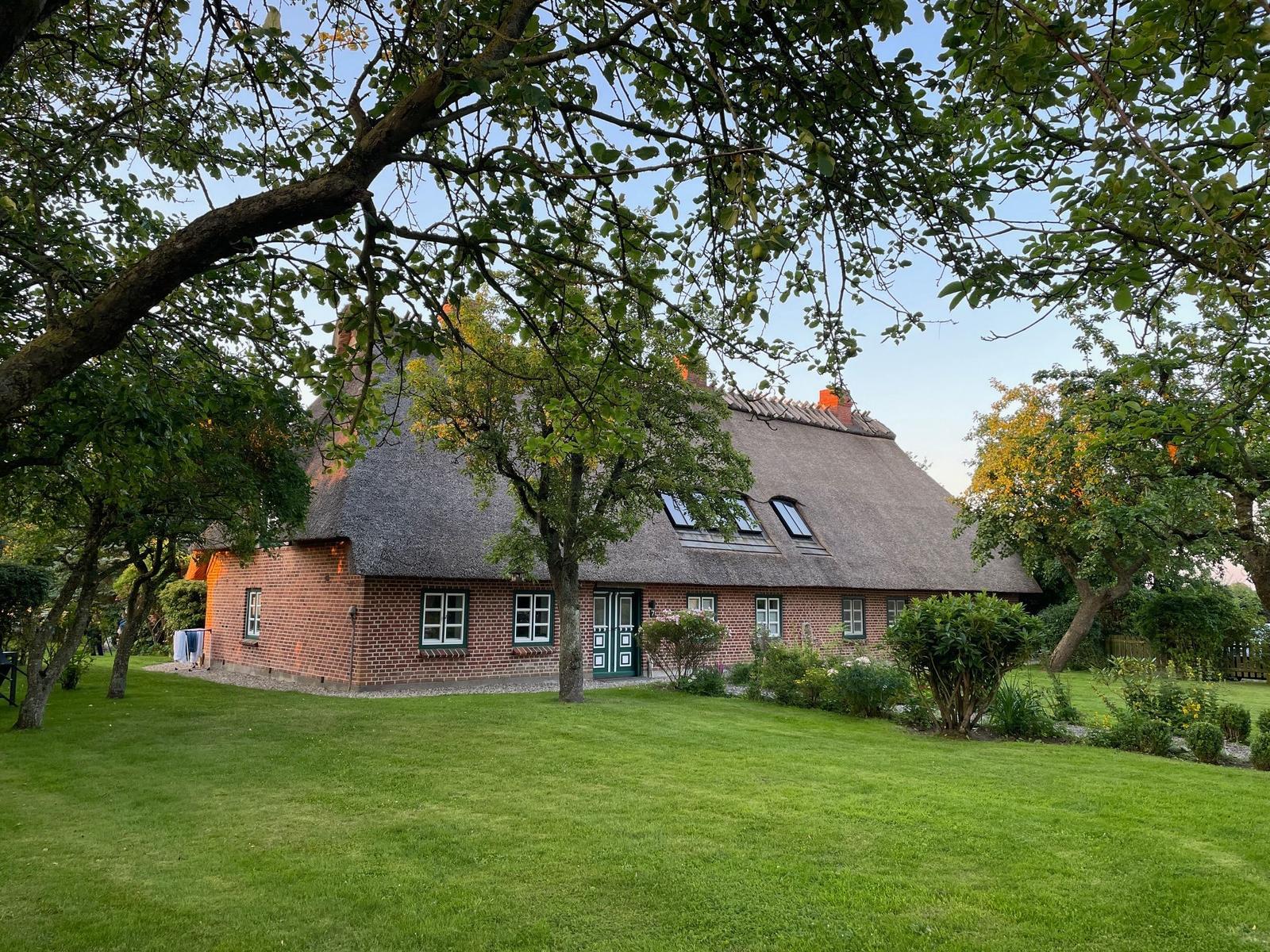 Haus mit Strohdach und Garten unter Bäumen.
