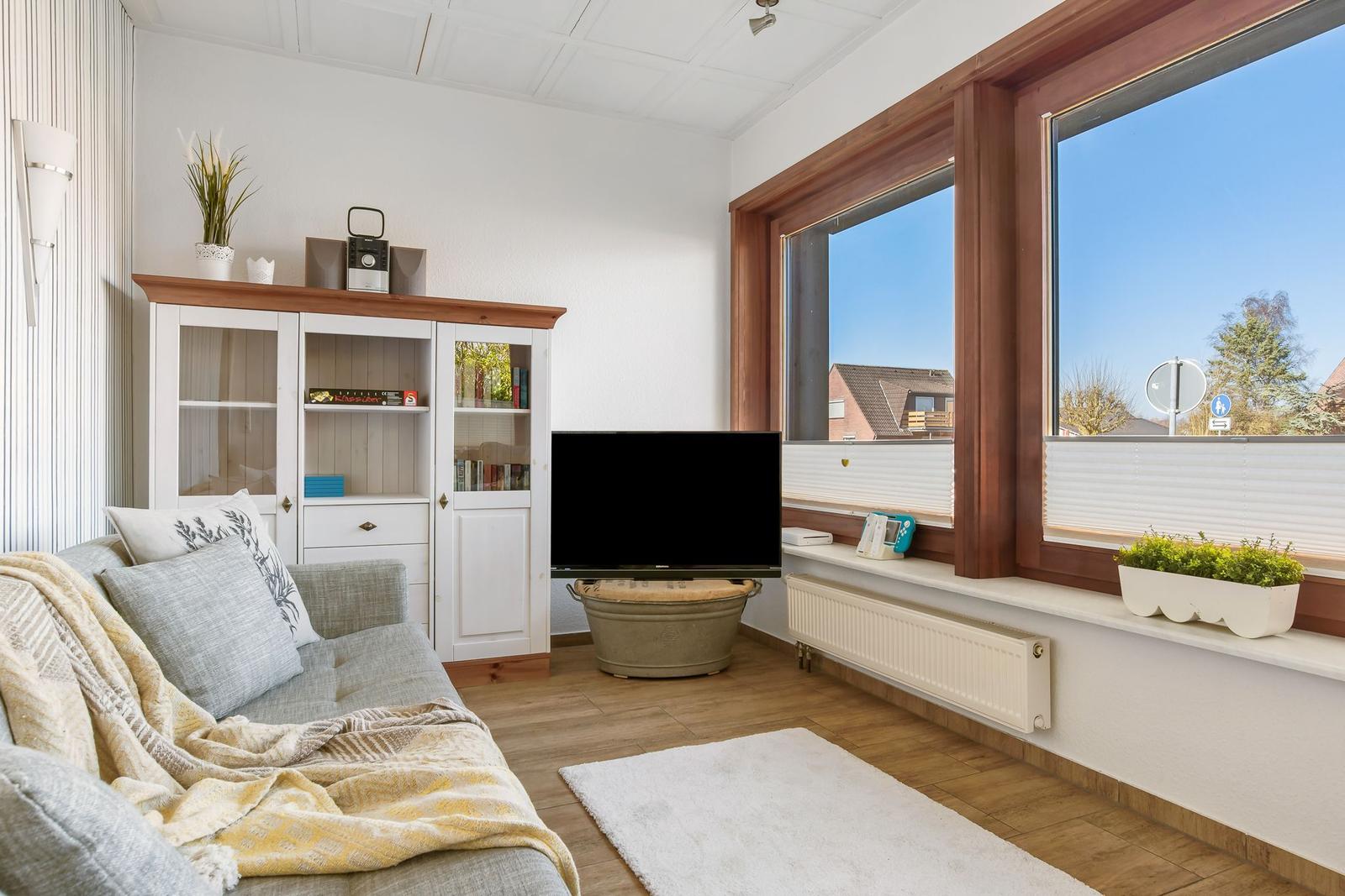Ein Raum mit großen Fenstern, Sofa, Stühlen und Blick auf Garten und Nachbarhäuser.