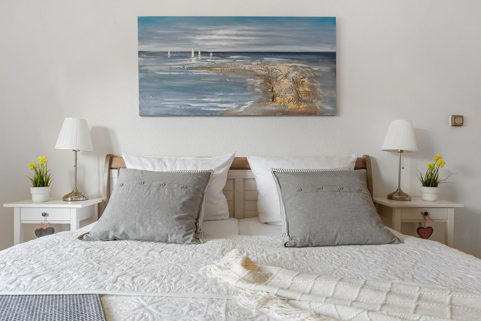 Schlafzimmer mit Bett, Wickerstuhl und Holztüren. Wandregal mit Blumen und Lautsprechern.