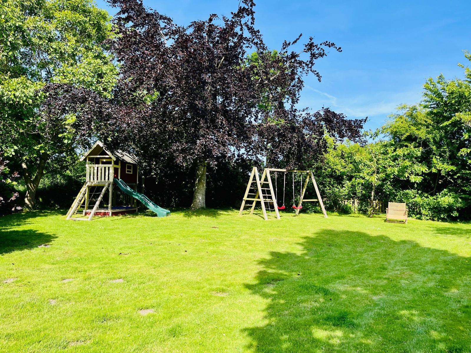 Hinterhof mit Spielplatz, Schaukel und Liegestuhl unter Bäumen.