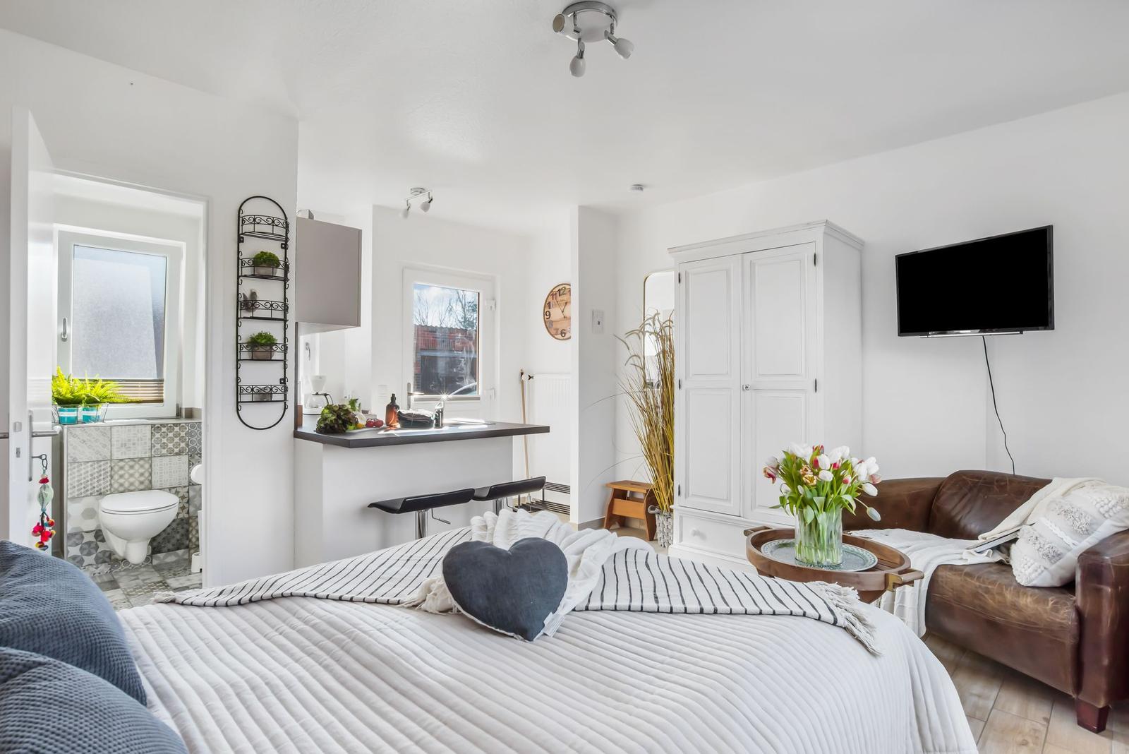 Schlafzimmer mit gestreifter Wand, Bett mit Kissen und Nachttischen mit Lampen.