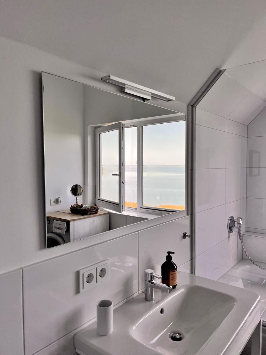 Durch das Fenster blickt man auf einen Strand und das Meer.