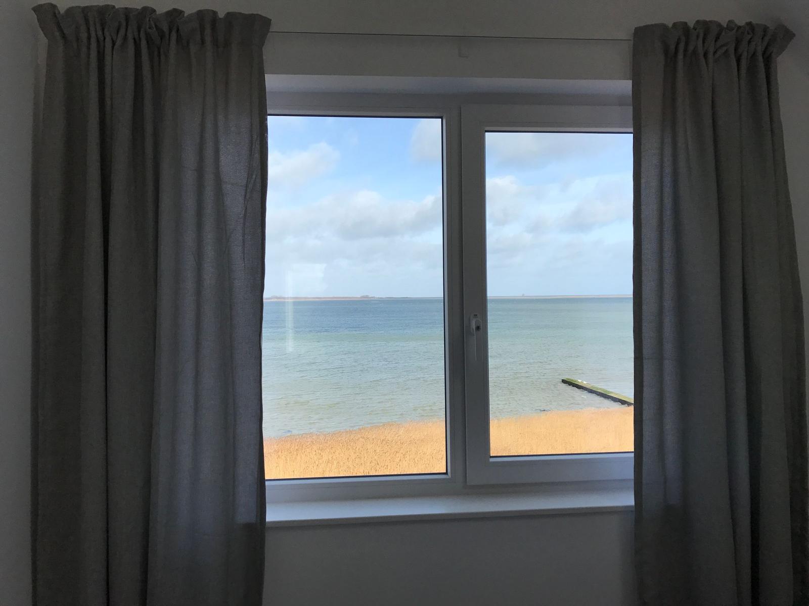Badezimmer mit Badewanne, Fensterblick auf Wasser, schwarze Fliesen und hängende Lampe.