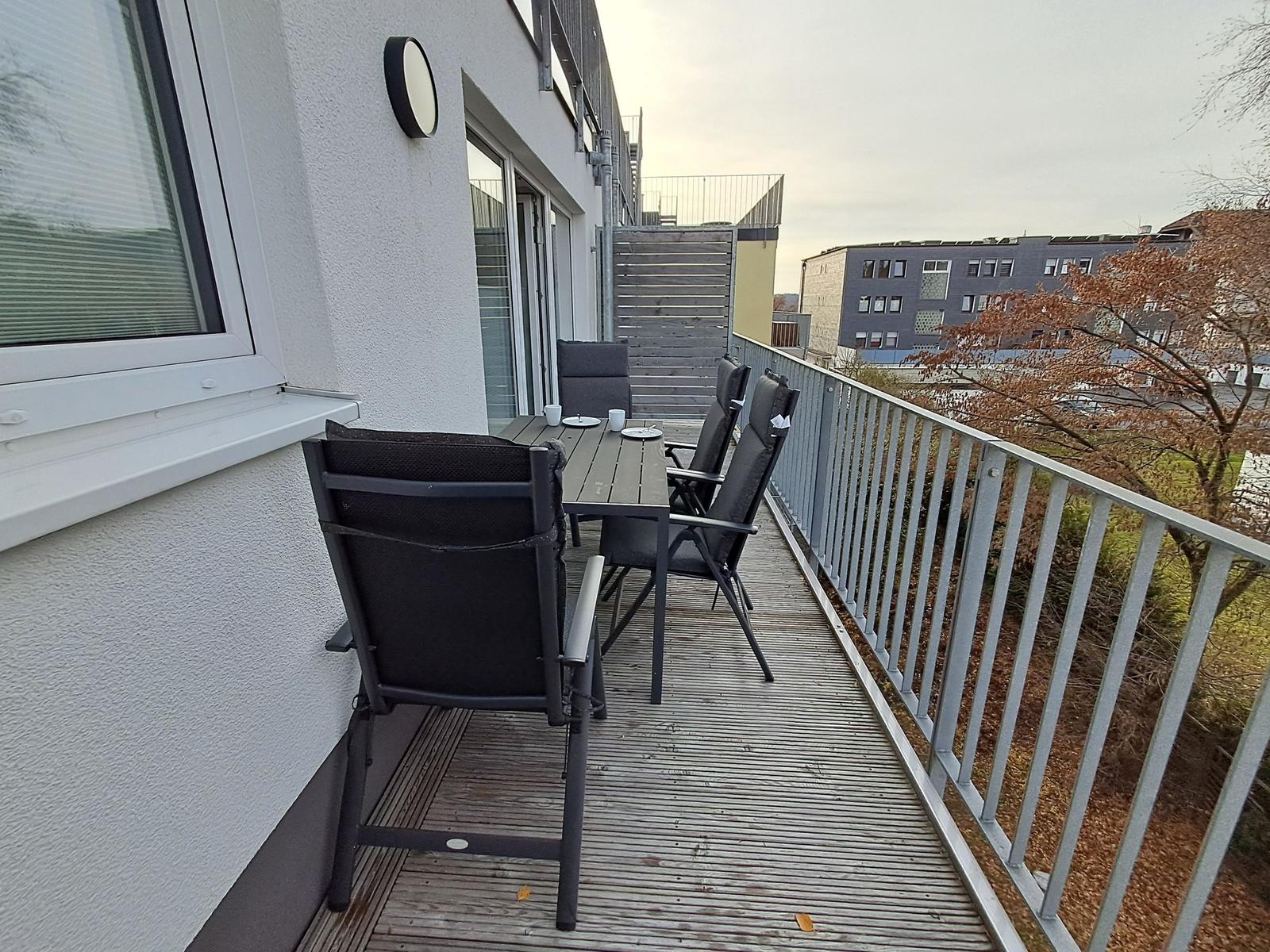 Terrasse mit Tisch und Stühlen. Blick auf Wohnhäuser und Grünflächen.