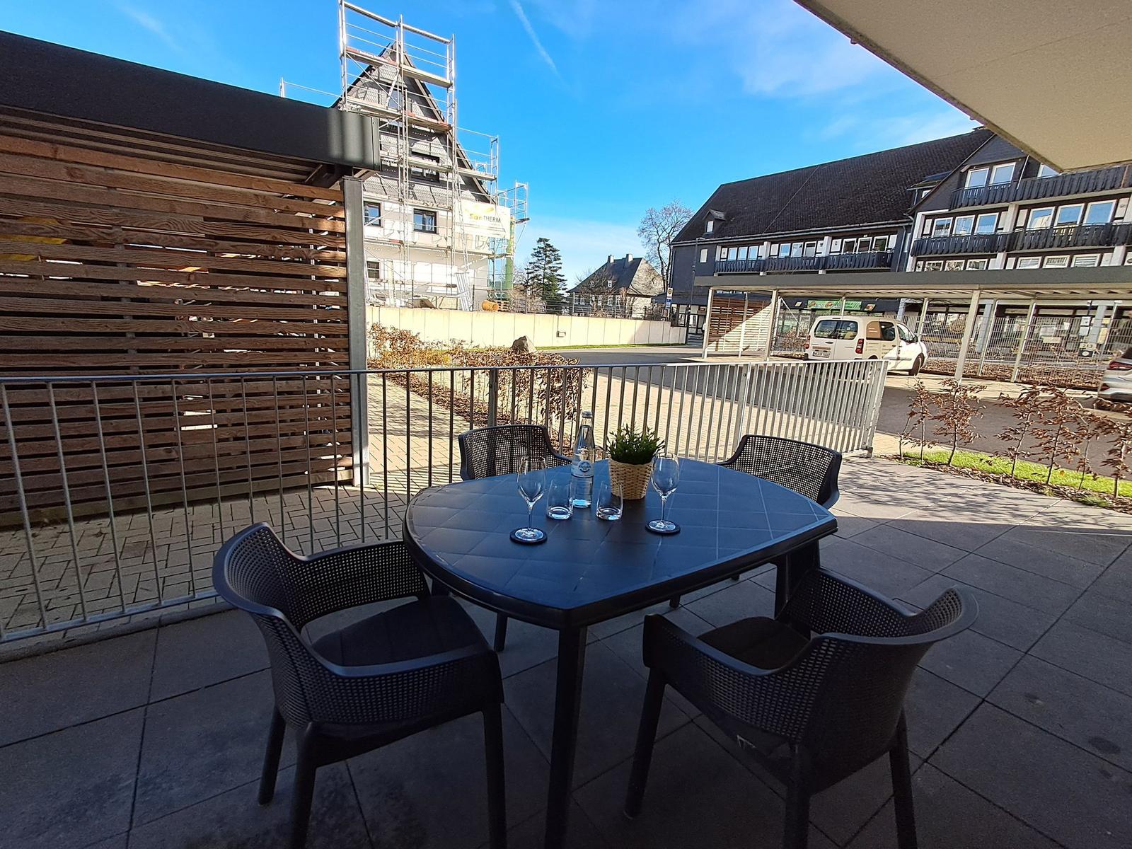 Terrasse mit Tisch und Stühlen, Blick auf Wohngebäude und Himmel.