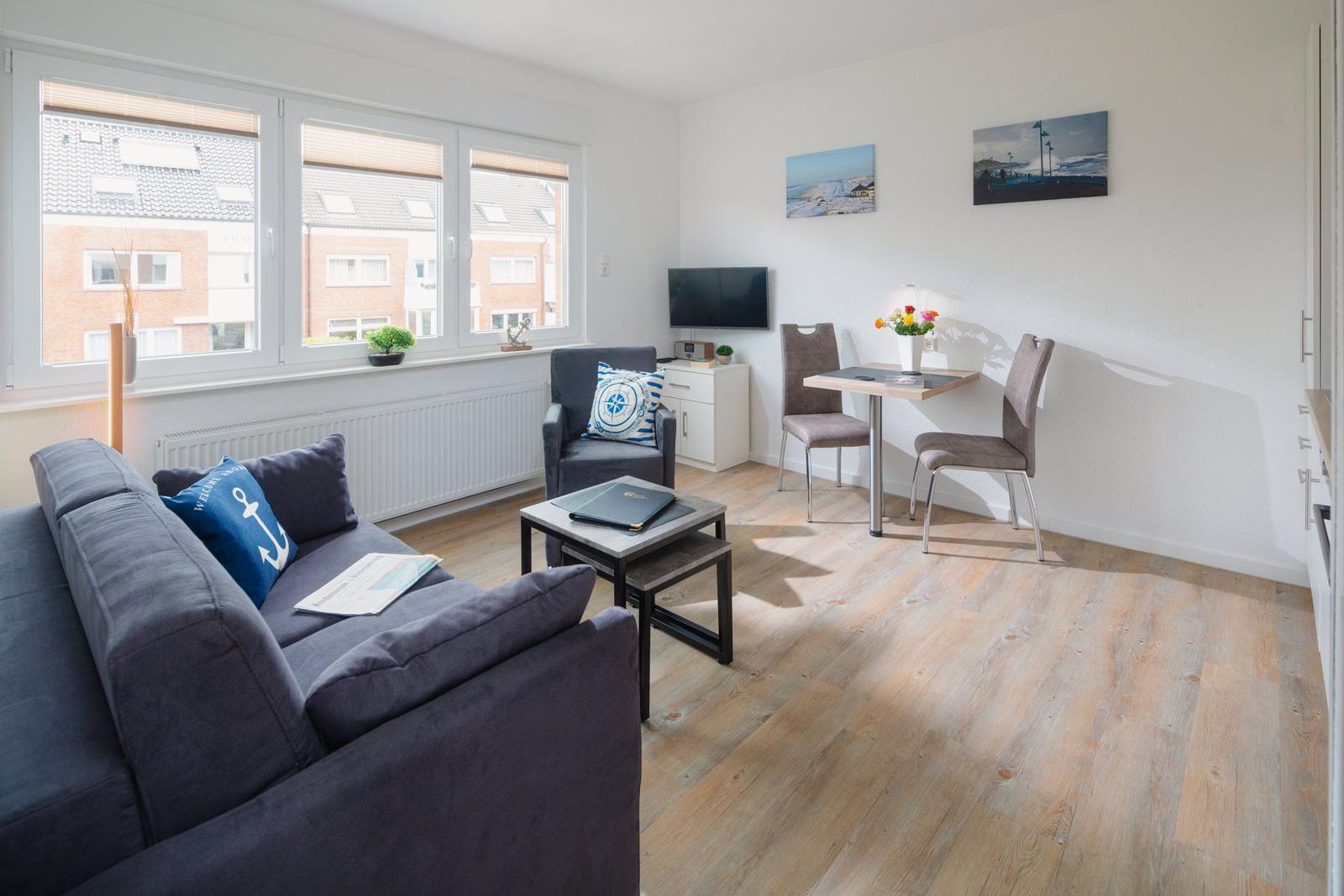Wohnung mit Küche, Sofa und Sessel. Holzboden und weiße Küchenmöbel.