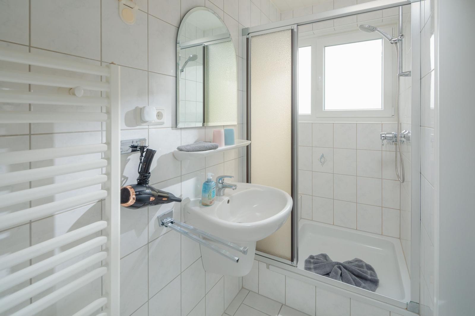 Badezimmer mit Toilette, Waschbecken und Heizkörper. Auf Regal Pflanze und Haartrockner.