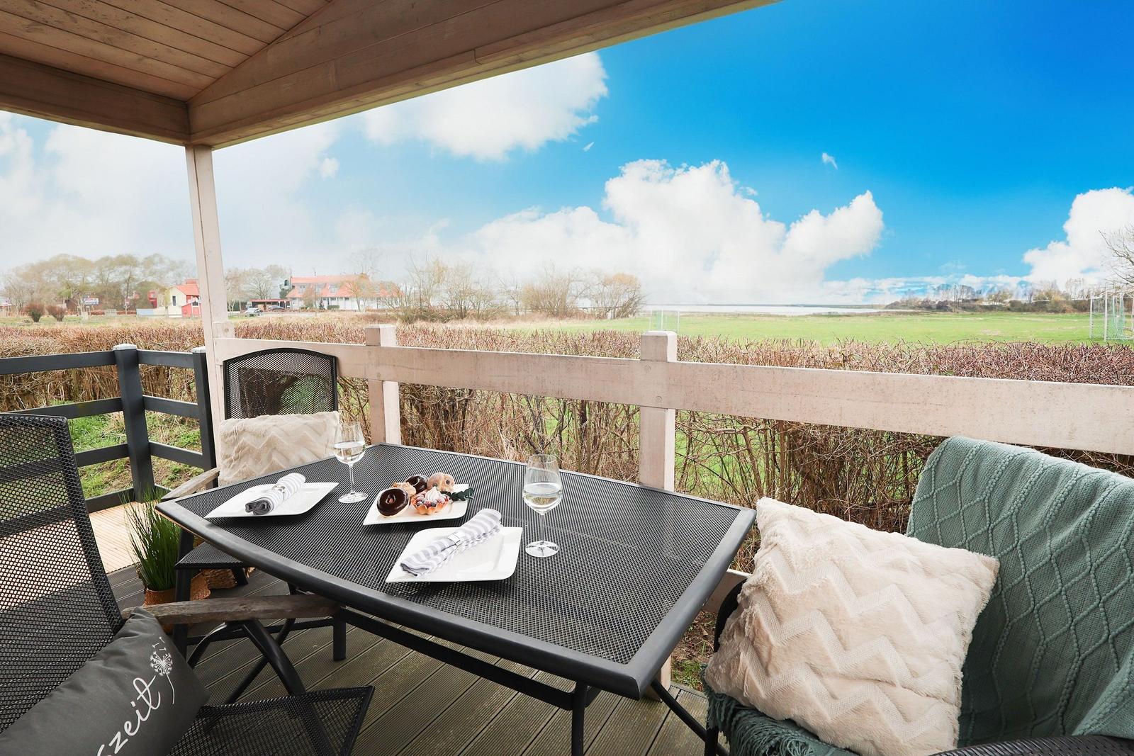 Terrace with table, chairs, and sea view. Sun is low on the horizon.