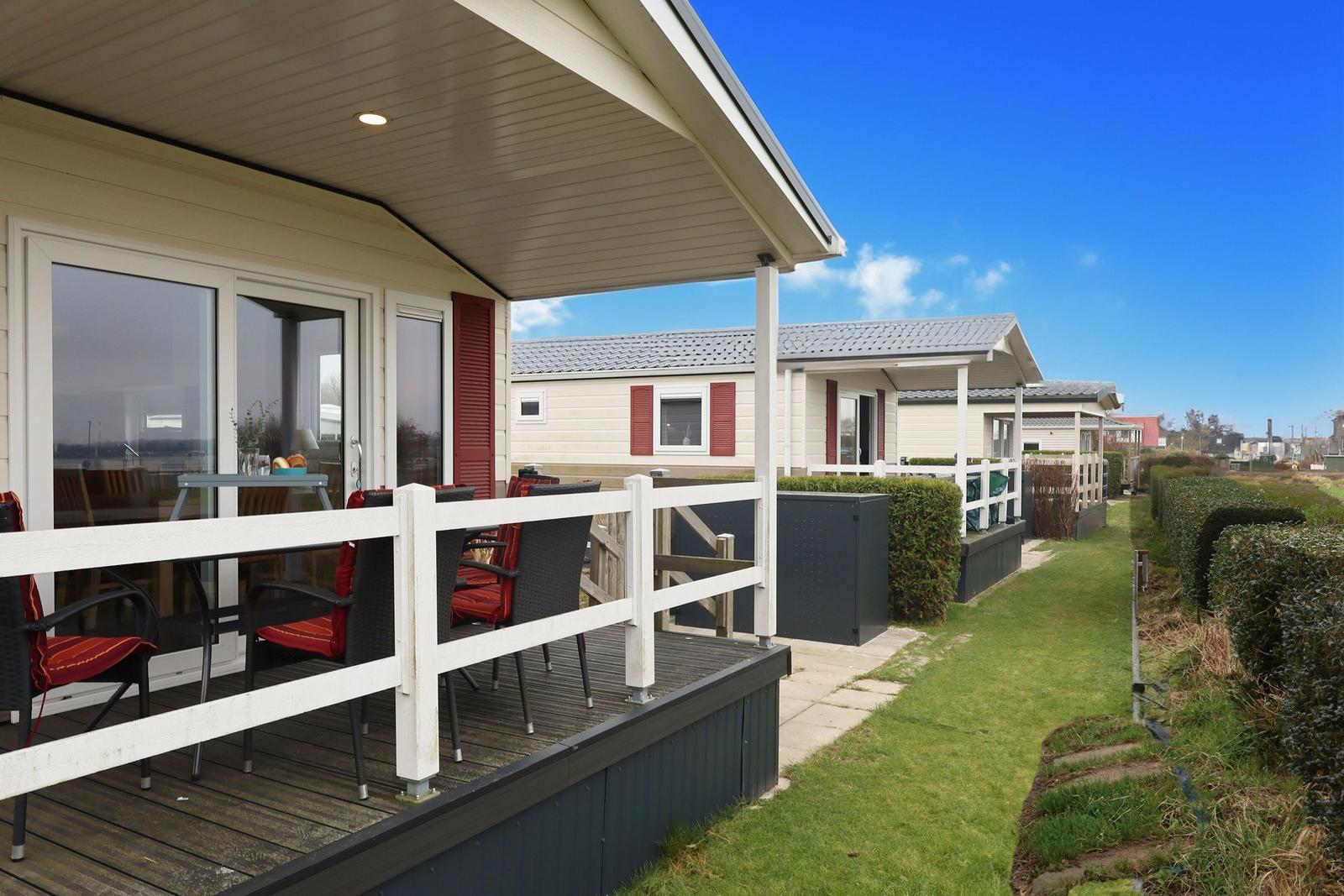 House with terrace, garden, and neighboring houses under blue sky.