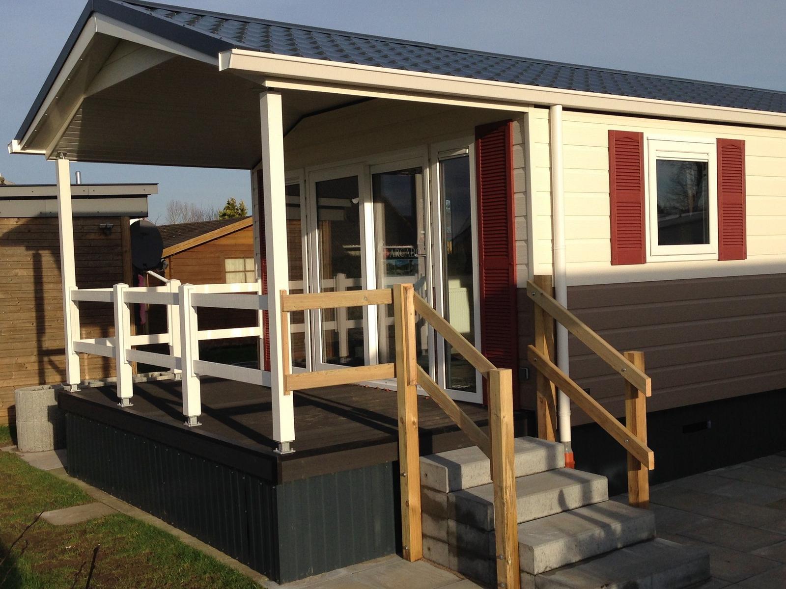 Two mobile homes with terrace and green garden under blue sky.
