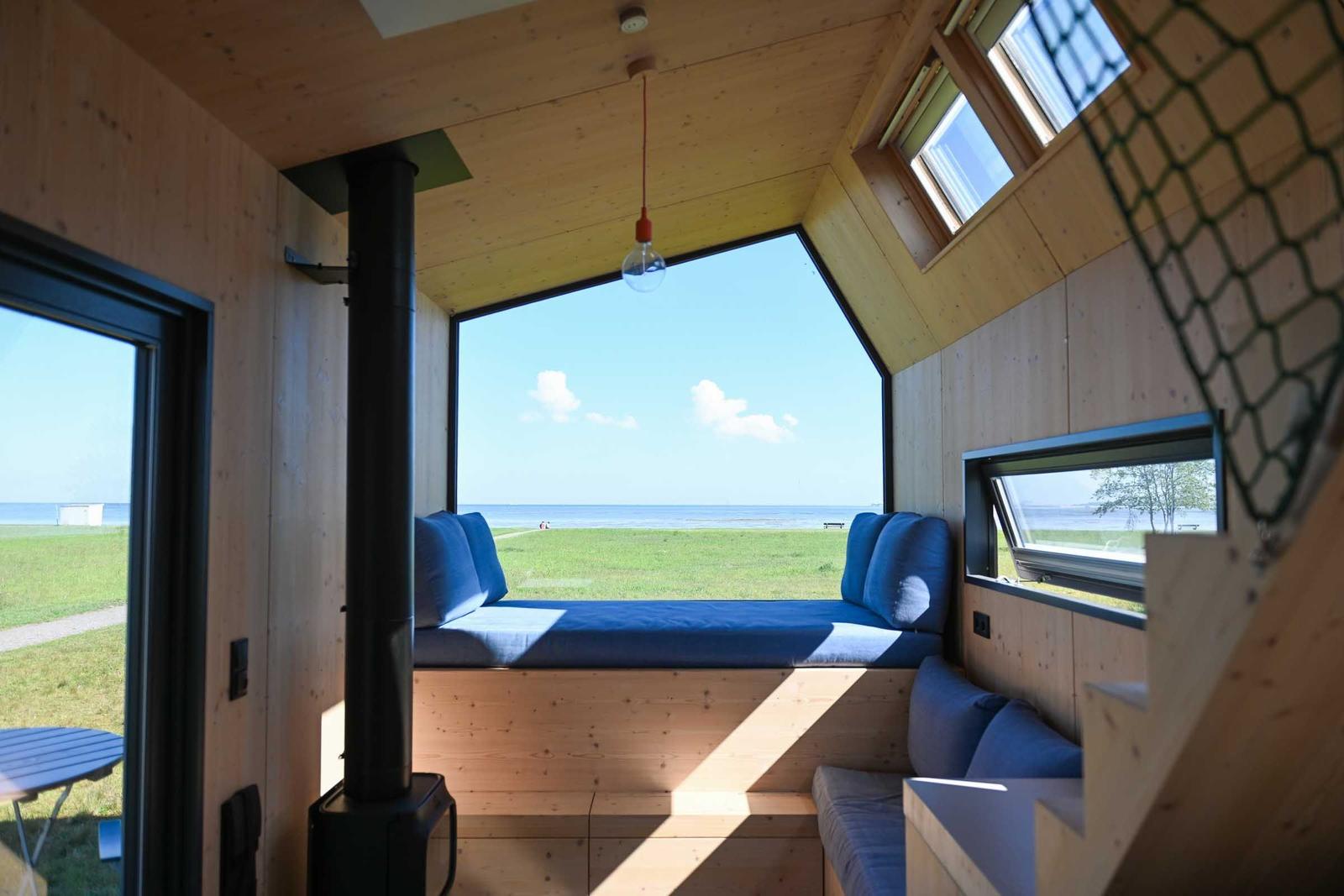 Holzveranda mit Tisch und Stühlen. Blick auf Grasland und Meer.