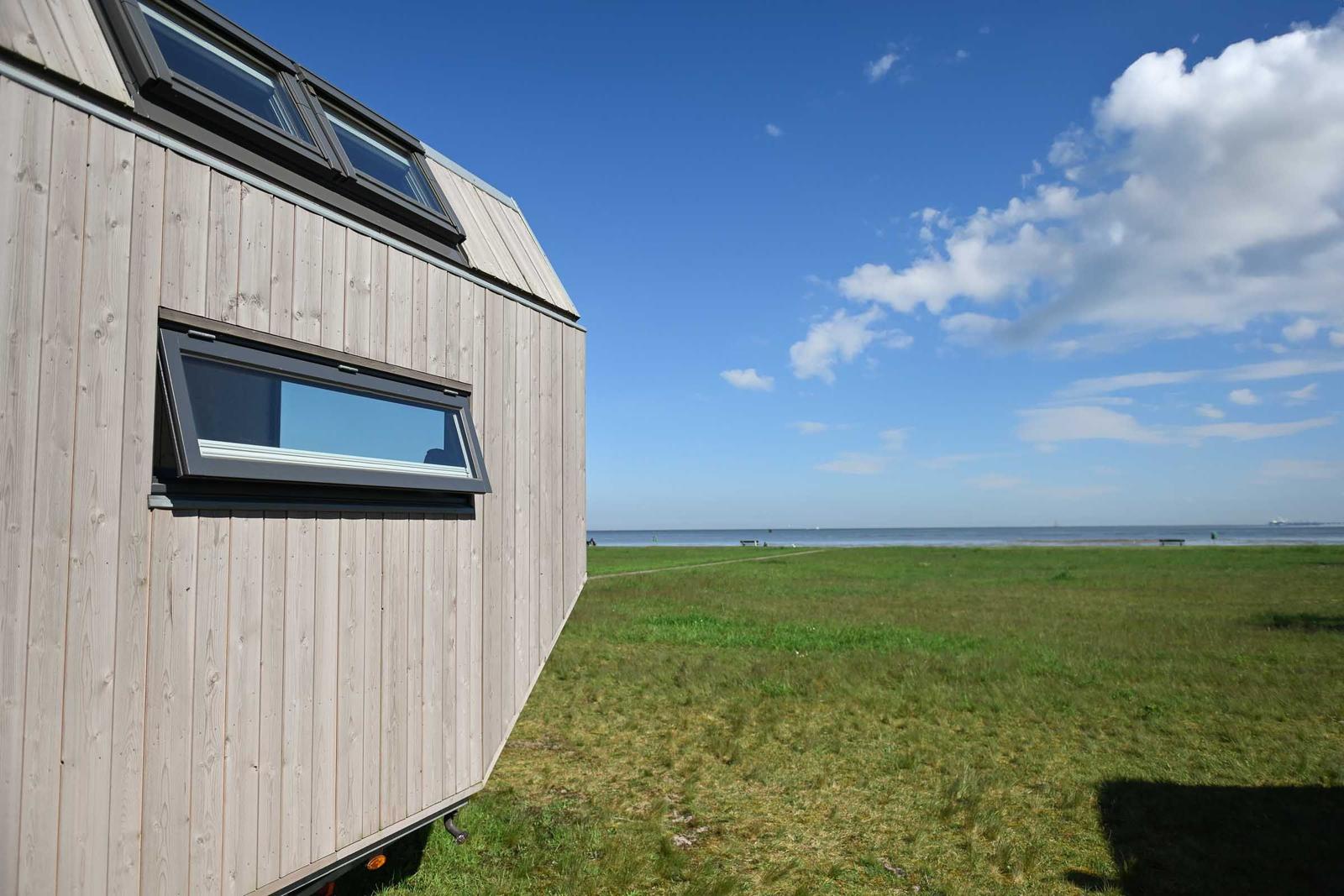 Holzhaus mit Terrasse, Tisch und Stühlen. Blick auf Wasser und Himmel.