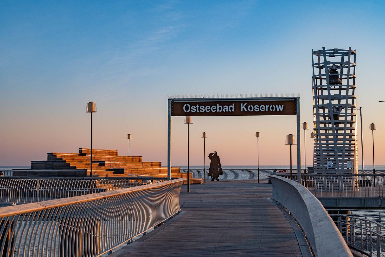 Strand mit Steg, wo Menschen spazieren gehen und das Meer genießen.