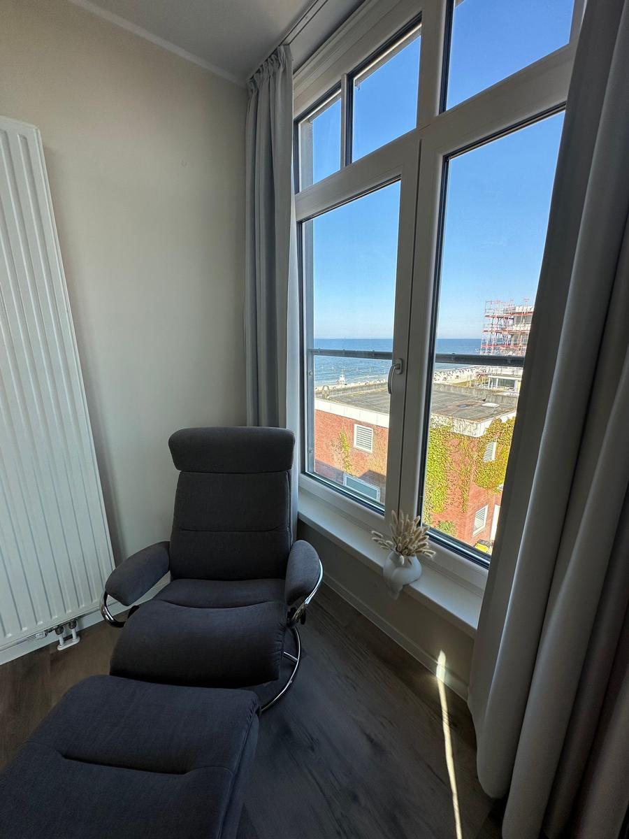 Wohnzimmer mit Sofa, Sessel und Fenster. Wand mit Bildern und Heizkörper.