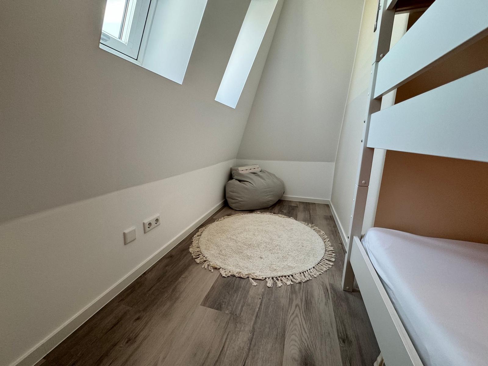 Zimmer mit Doppelstockbett, Holzboden und Fenster im Hintergrund.
