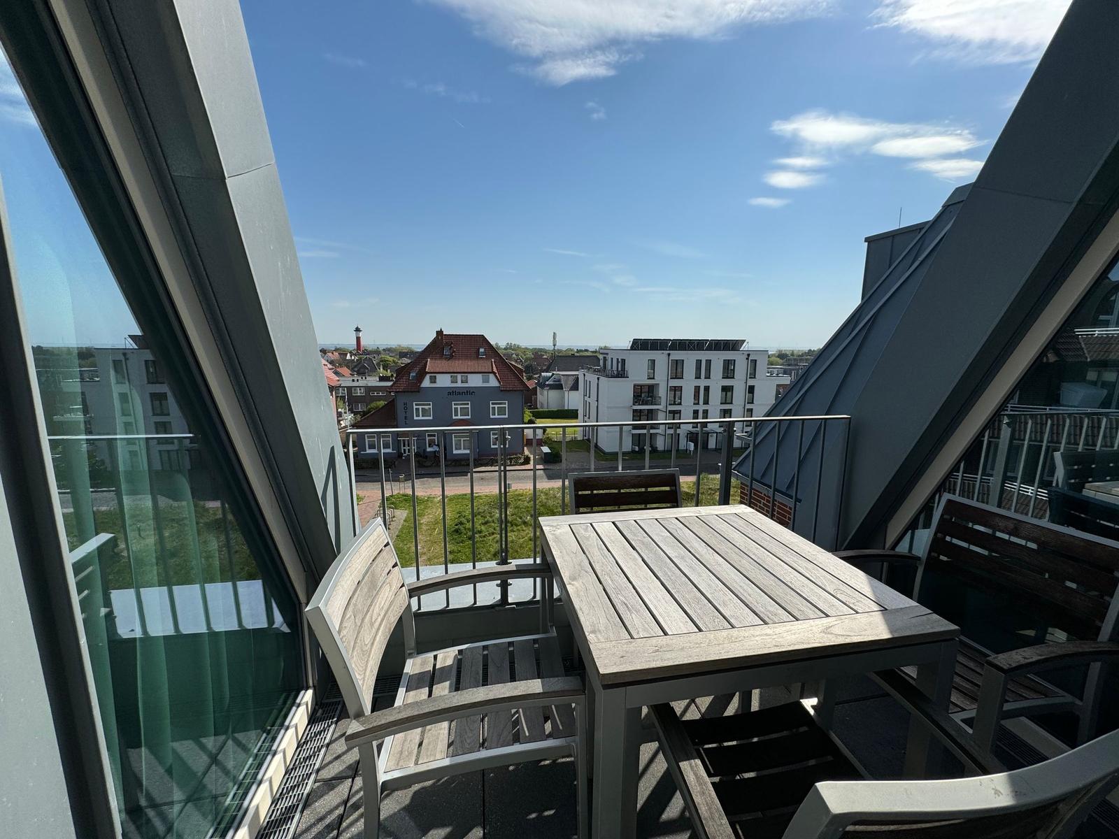 Terrasse mit Blick auf blaues Hotel und Leuchtturm im Hintergrund.