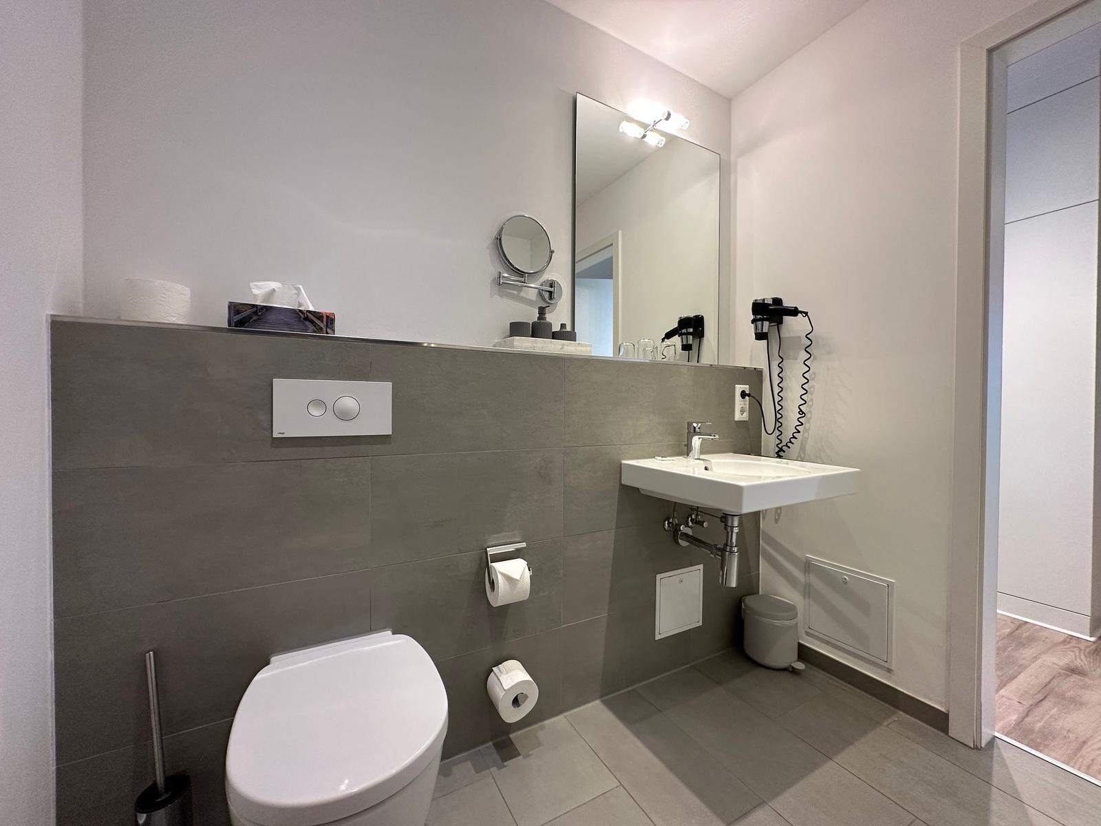 Badezimmer mit Toilette, Waschbecken und Heizkörper. Wandspiegel und Pflanze sichtbar.