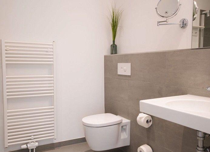 Dusche mit Glaswand, grauen Fliesen und Handtuch auf Boden